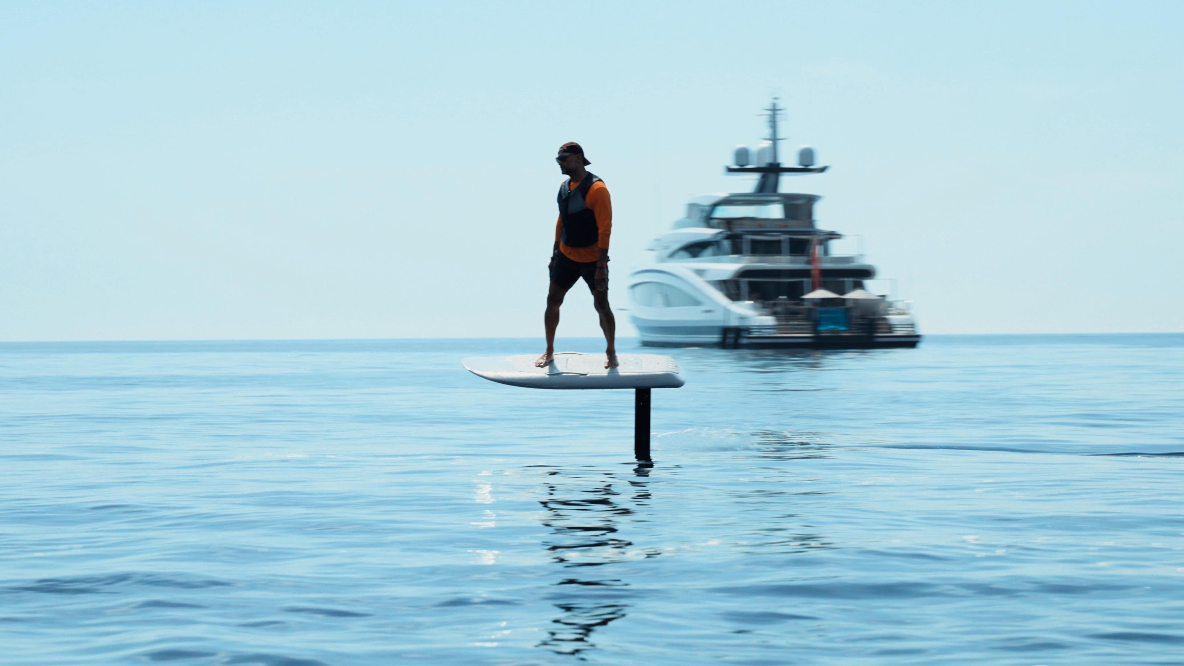 eFoil rider gliding on calm open water with a superyacht anchored behind
